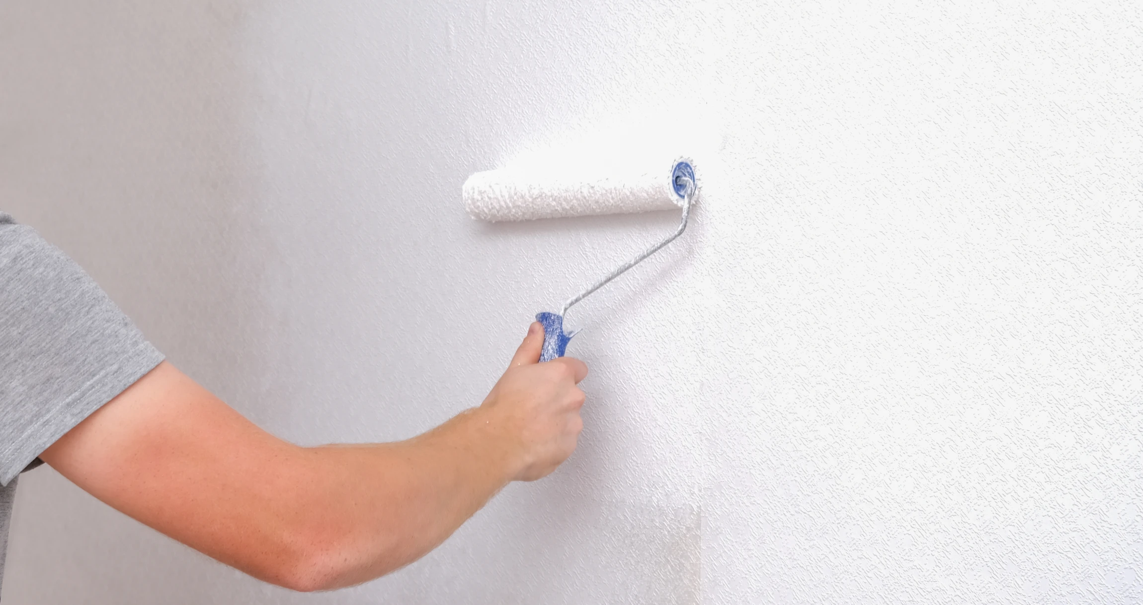 Personne appliquant de la peinture blanche sur un mur intérieur à l'aide d'un rouleau à peinture