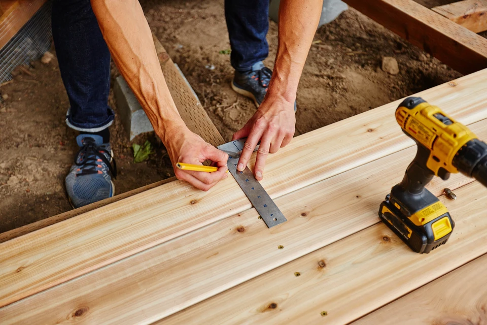 Artisan menuisier travaillant dans un atelier, utilisant un crayon de menuisier pour tracer des mesures précises sur une planche de bois