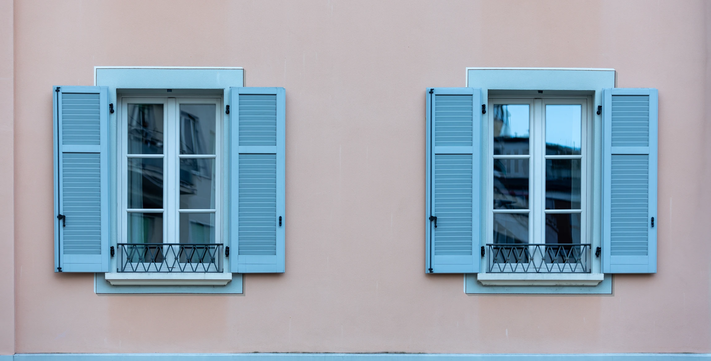 Un peintre en bâtiment applique de la peinture rose sur un mur extérieur blanc à l'aide d'un rouleau à poils